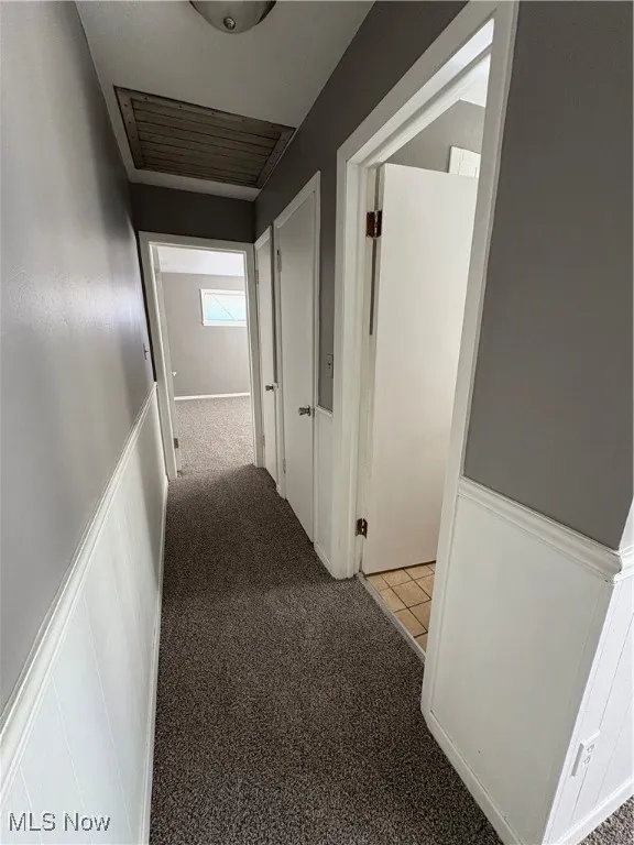 Hallway with light carpet and a wainscoted wall