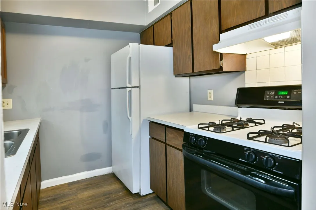 Kitchen with gas range oven, under cabinet range hood, light countertops, dark wood-style flooring, and freestanding refrigerator