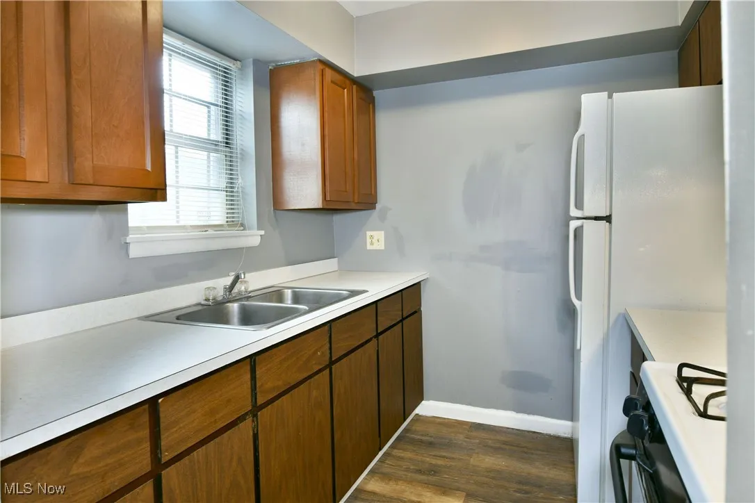 Kitchen featuring white range oven, dark wood finished floors, light countertops, and brown cabinets