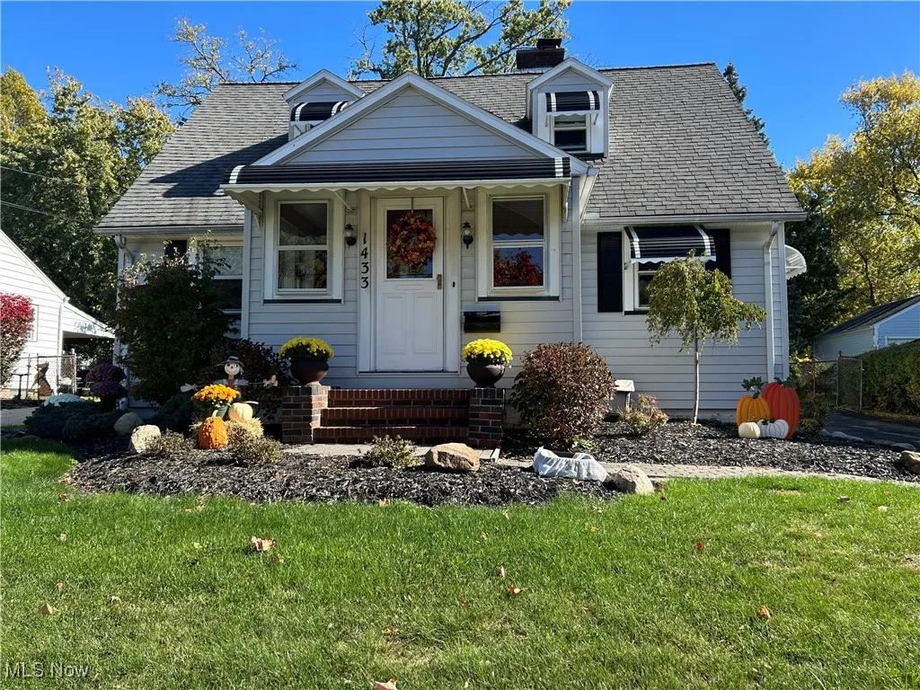 View of front of property featuring a front yard, covered porch, a shingled roof, and a chimney