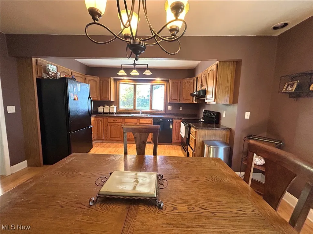 Kitchen featuring black appliances, pendant lighting, light wood finished floors, a chandelier, and brown cabinets
