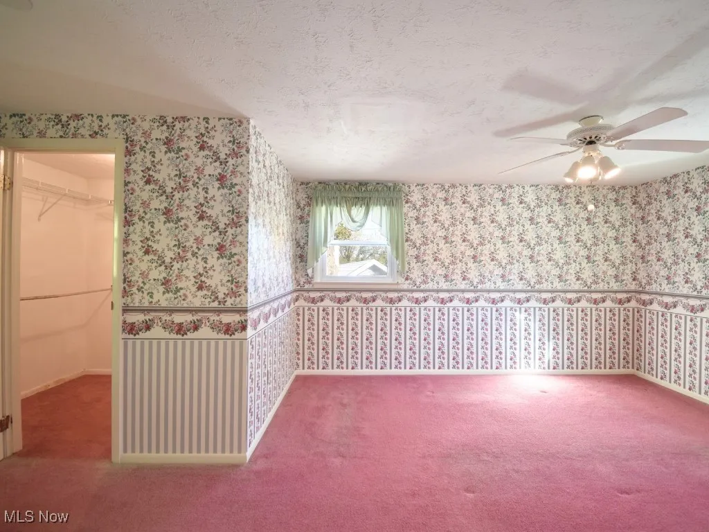 Unfurnished room featuring a textured ceiling, carpet, and ceiling fan