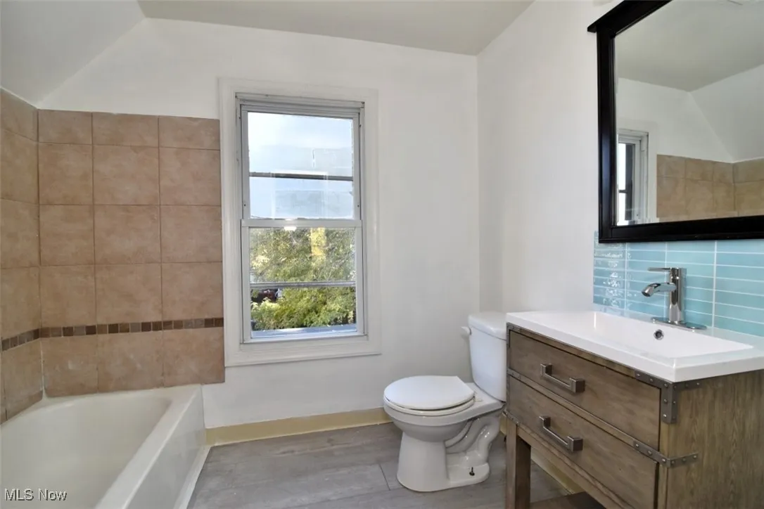 Bathroom with a tub, vanity, decorative backsplash, light wood-style floors, and vaulted ceiling