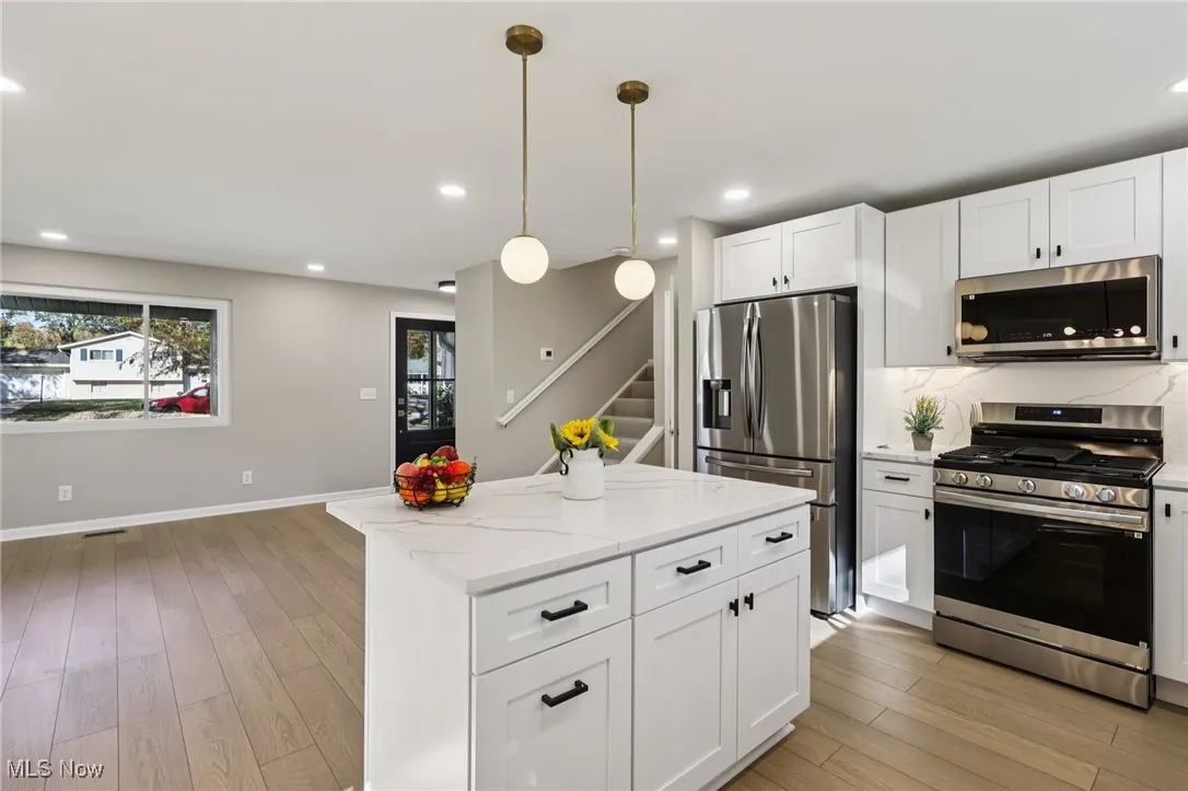 Kitchen featuring appliances with stainless steel finishes, white cabinets, light wood-style flooring, decorative light fixtures, and a kitchen island
