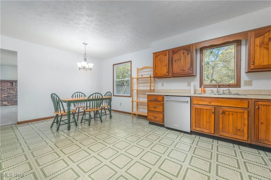 Kitchen with brown cabinets, light countertops, stainless steel dishwasher, a textured ceiling, and hanging light fixtures