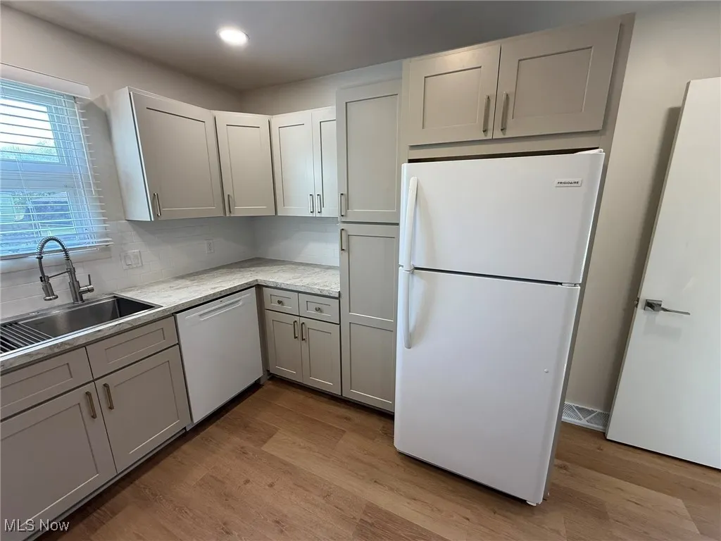 Kitchen featuring white appliances, light wood finished floors, gray cabinetry, light stone counters, and decorative backsplash
