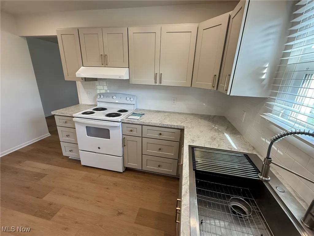 Kitchen featuring electric stove, light wood-style flooring, light stone counters, tasteful backsplash, and under cabinet range hood