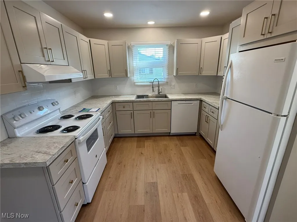 Kitchen with white appliances, gray cabinets, light countertops, light wood-style floors, and under cabinet range hood