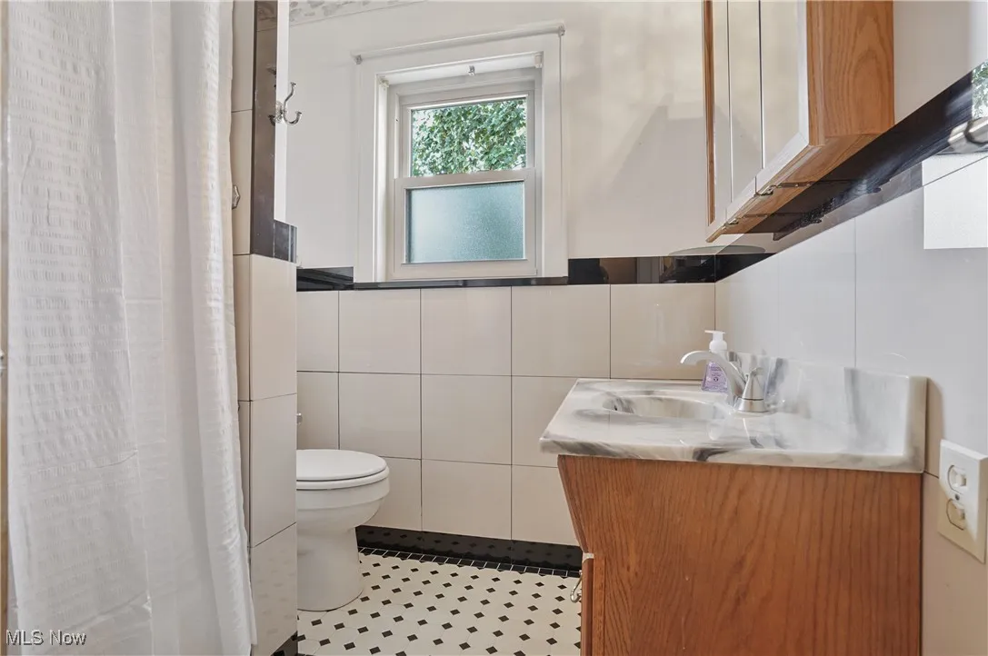 Bathroom with a shower with curtain, vanity, tile walls, and light tile patterned floors
