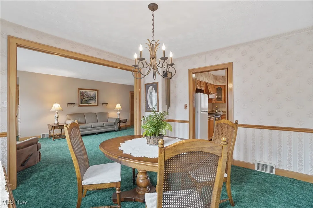 Dining area featuring wallpapered walls, carpet, and a chandelier
