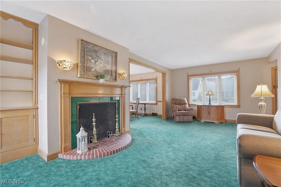 Carpeted living room featuring a fireplace with raised hearth and baseboards