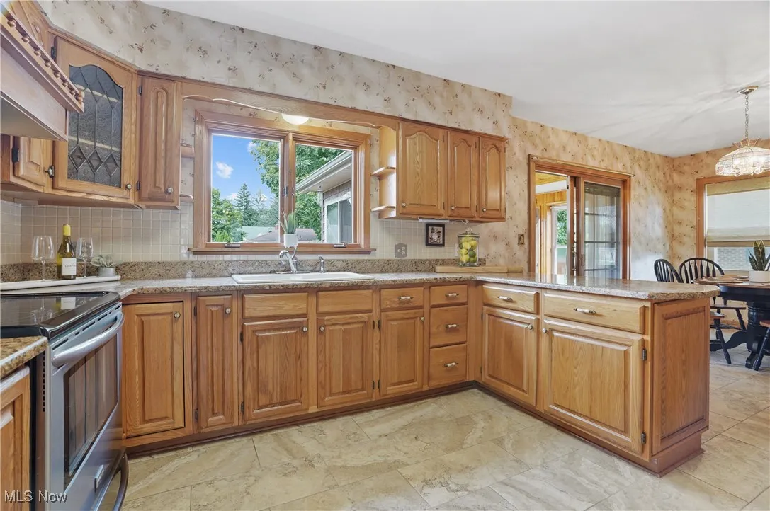 Kitchen featuring wallpapered walls, brown cabinets, electric range, plenty of natural light, and a peninsula