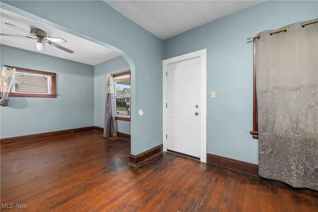 Empty room featuring dark wood-style flooring, arched walkways, and a ceiling fan