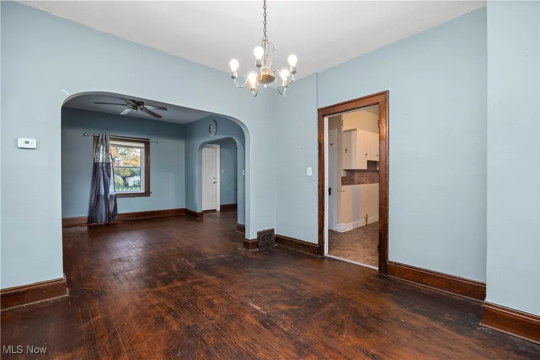 Empty room featuring arched walkways, dark wood-style floors, a ceiling fan, and a chandelier