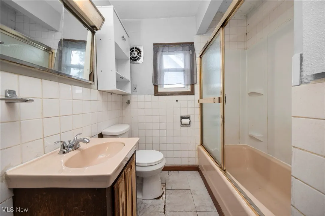 Full bath featuring vanity, shower / bath combination with glass door, tile walls, and light tile patterned flooring