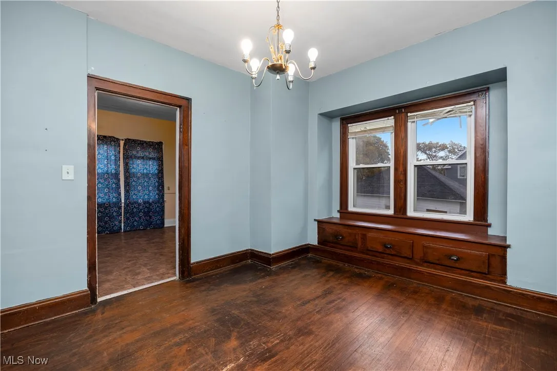 Empty room featuring dark wood-style flooring and a chandelier