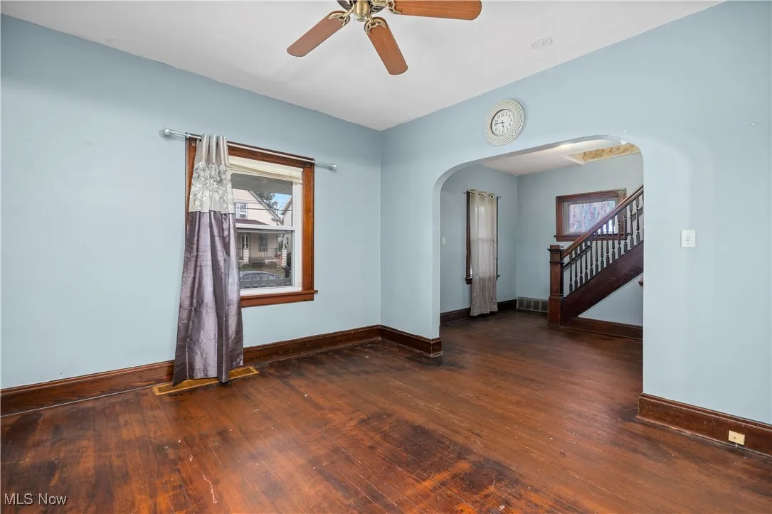 Unfurnished room with dark wood-style floors, stairs, a ceiling fan, and arched walkways