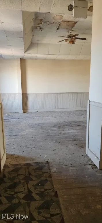 Unfurnished room with a paneled ceiling, wainscoting, and a ceiling fan