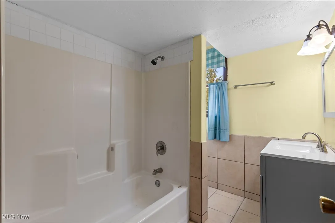 Full bath with vanity, tile walls, light tile patterned floors, shower / bath combination, and a textured ceiling