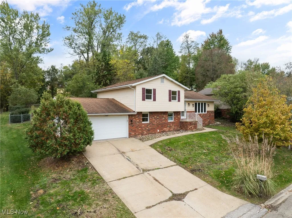 Tri-level home with brick veneer,  siding, a front lawn, concrete driveway, a garage, and a shingled roof