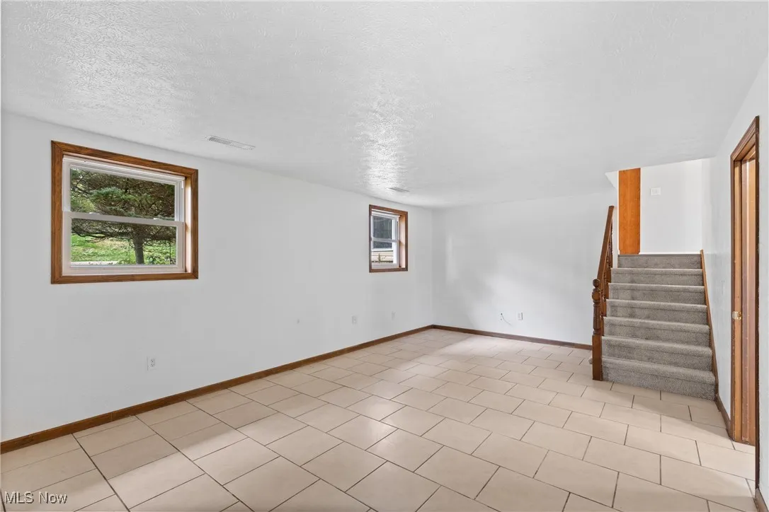 Below grade area featuring plenty of natural light, a textured ceiling, stairs, and light tile patterned floors