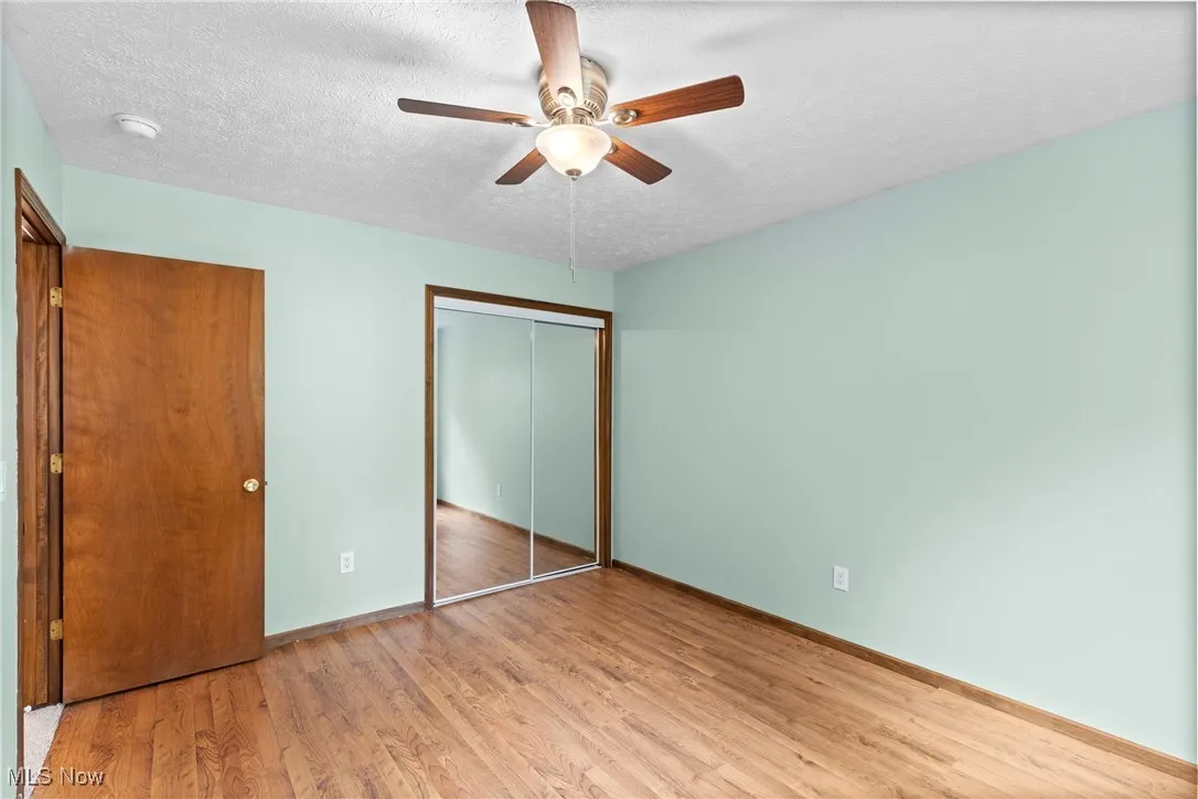Unfurnished bedroom featuring light wood-type flooring, a closet, a textured ceiling, and a ceiling fan