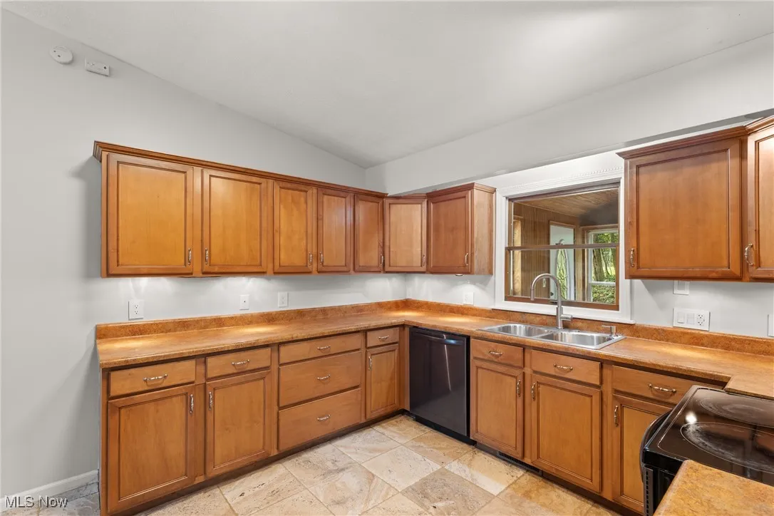 Kitchen with brown cabinetry, stainless appliances, light countertops, and light stone tile flooring