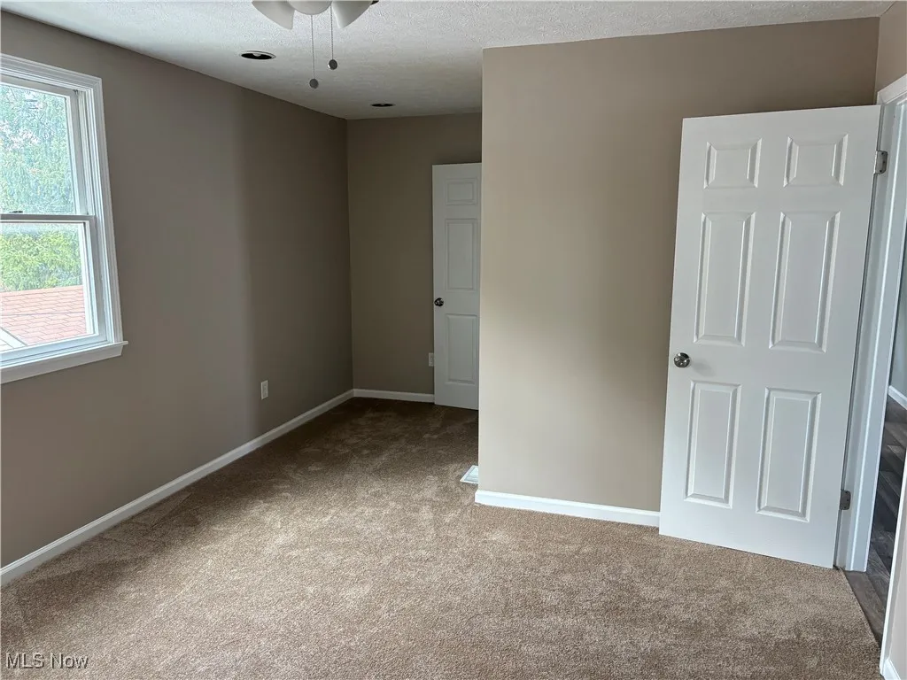 Unfurnished room featuring a textured ceiling, light carpet, and a ceiling fan