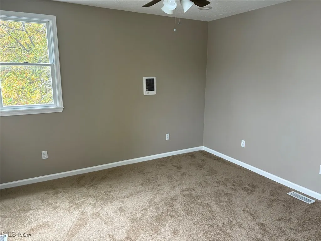 Unfurnished room featuring light colored carpet, a textured ceiling, and ceiling fan