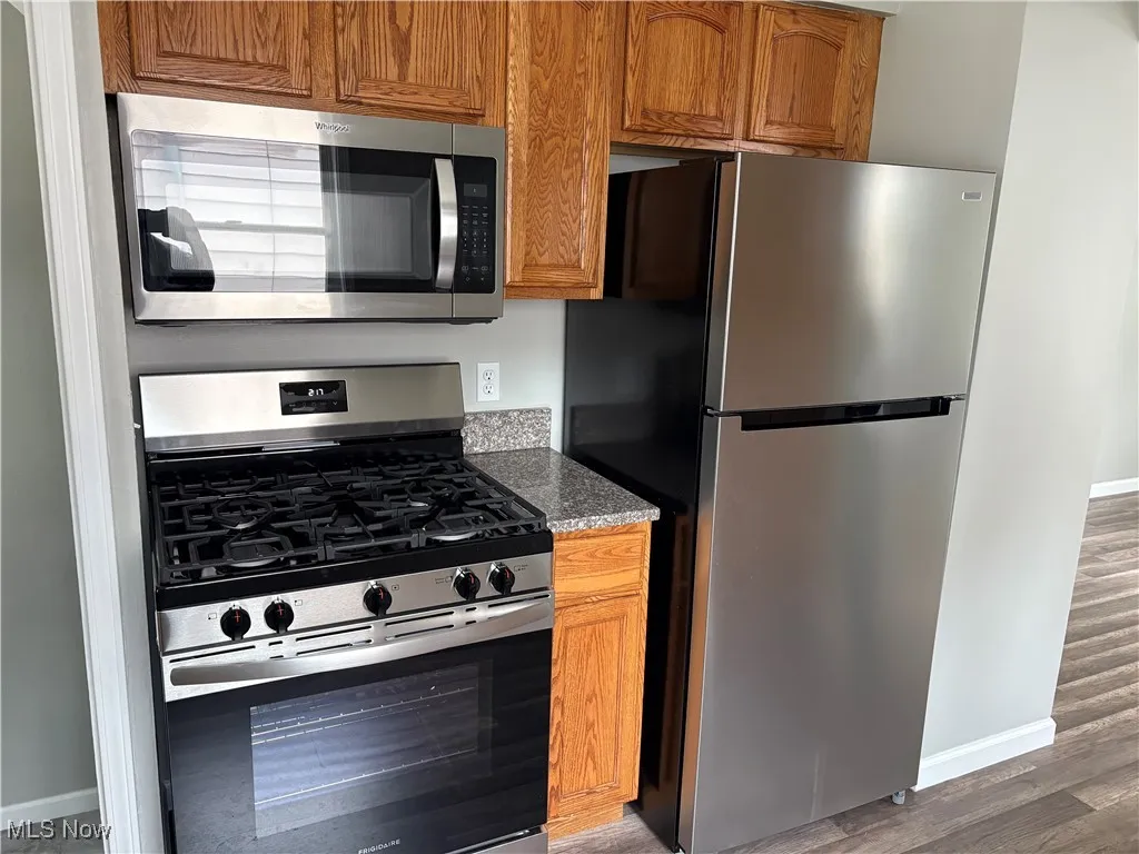 Kitchen with stainless steel appliances, brown cabinetry, light wood finished floors, and light stone countertops