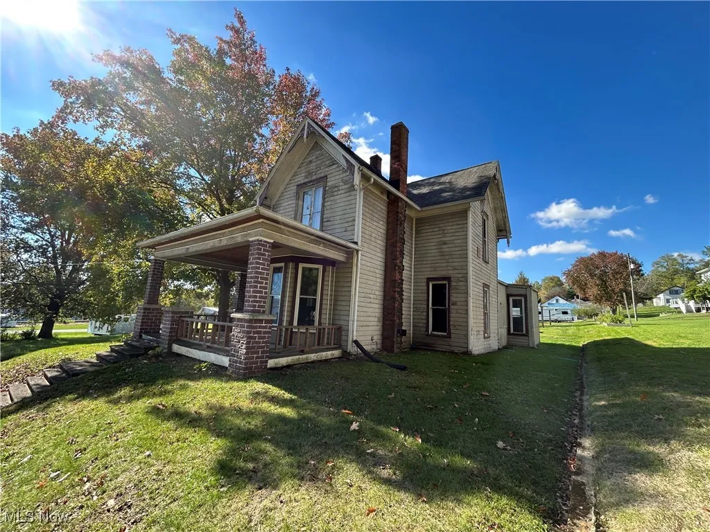 View of side of property with a yard, a chimney, and covered porch