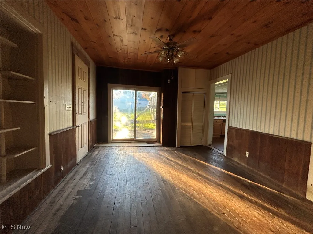 Spare room with wooden walls, hardwood / wood-style floors, wainscoting, healthy amount of natural light, and a ceiling fan