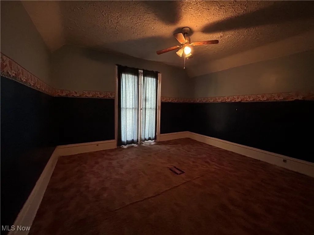 Spare room with lofted ceiling, a textured ceiling, dark carpet, and a ceiling fan