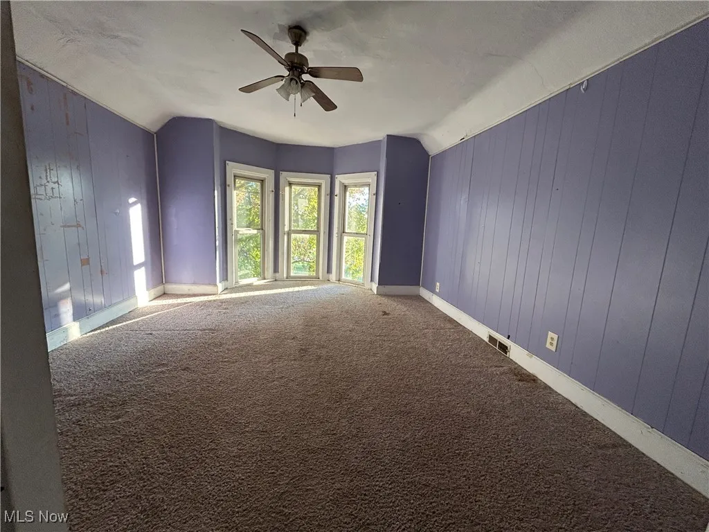 Empty room with wooden walls, carpet, a ceiling fan, and lofted ceiling