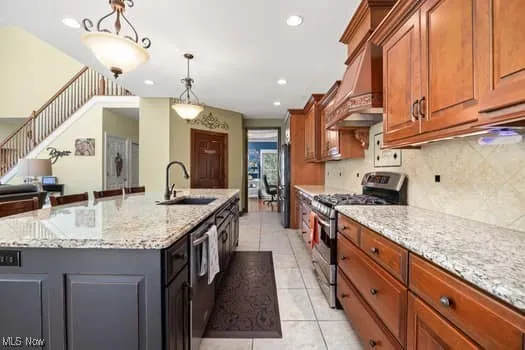 Kitchen featuring appliances with stainless steel finishes, light tile patterned floors, pendant lighting, light stone counters, and custom exhaust hood