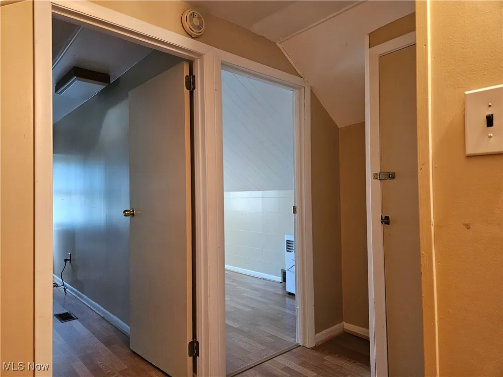 Corridor with wood finished floors and vaulted ceiling