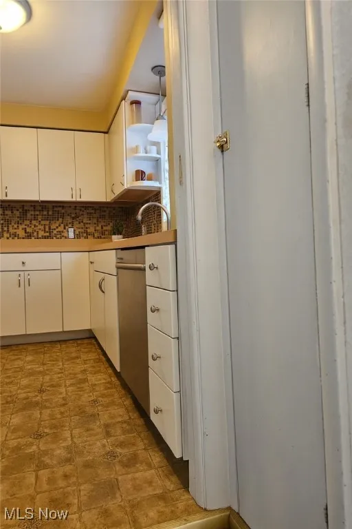 Kitchen featuring tasteful backsplash, white cabinetry, open shelves, light countertops, and decorative light fixtures