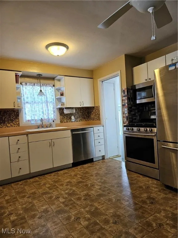 Kitchen with white cabinets, open shelves, tasteful backsplash, refrigerator, and stove
