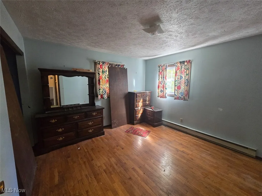 Bedroom with baseboard heating, wood-type flooring, and a textured ceiling