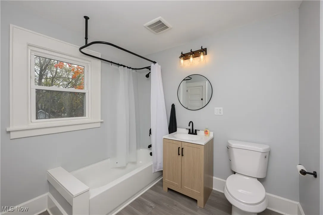 Full bathroom with shower / bathtub combination with curtain, vanity, and light wood-style floors