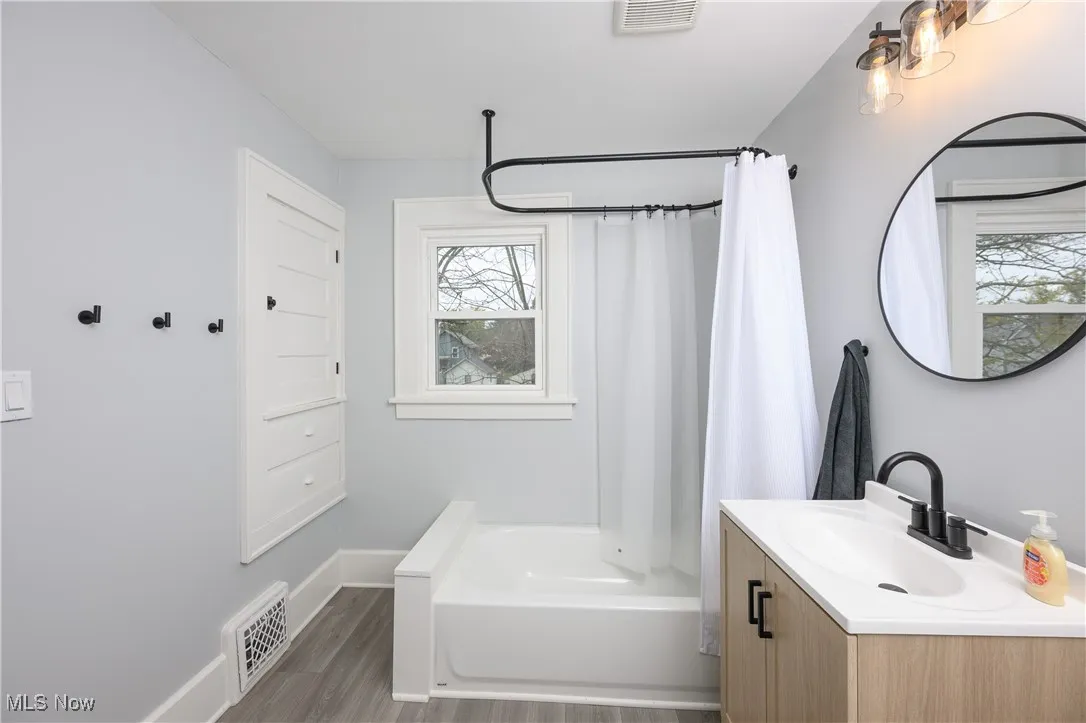 Full bath with shower / bath combo with shower curtain, vanity, and wood finished floors