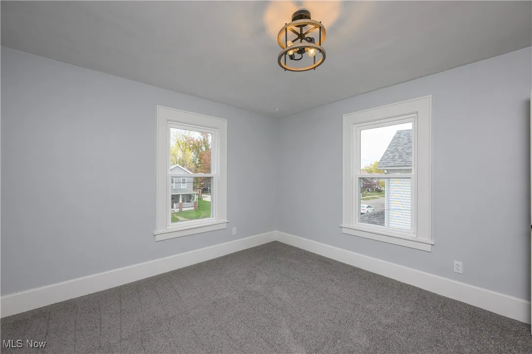 Carpeted empty room featuring baseboards and a chandelier