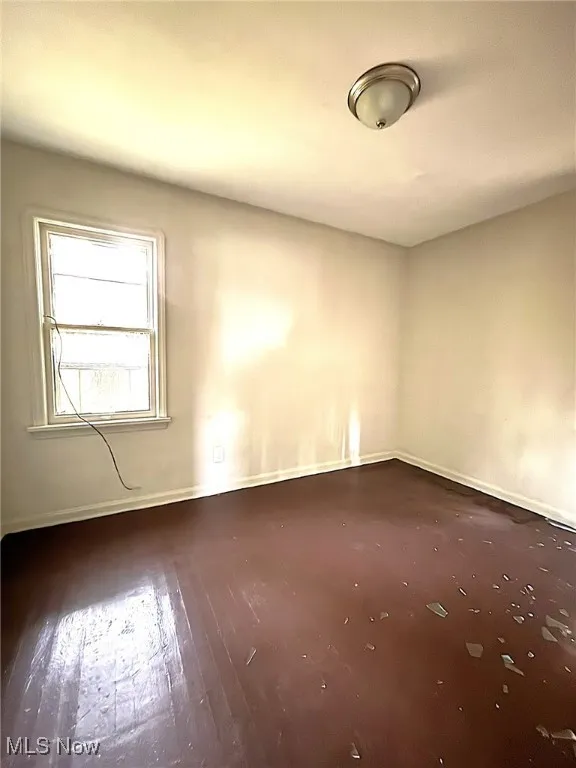 Spare room featuring baseboards and dark wood-style flooring