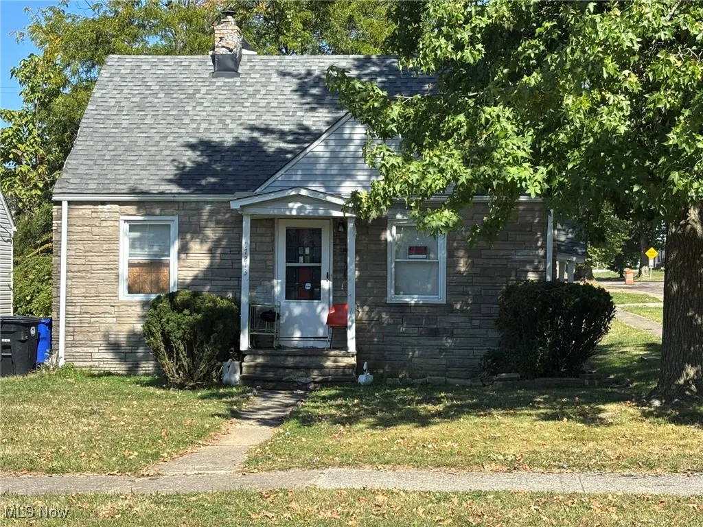 View of front of house featuring stone siding, a front lawn, roof with shingles, and a chimney
