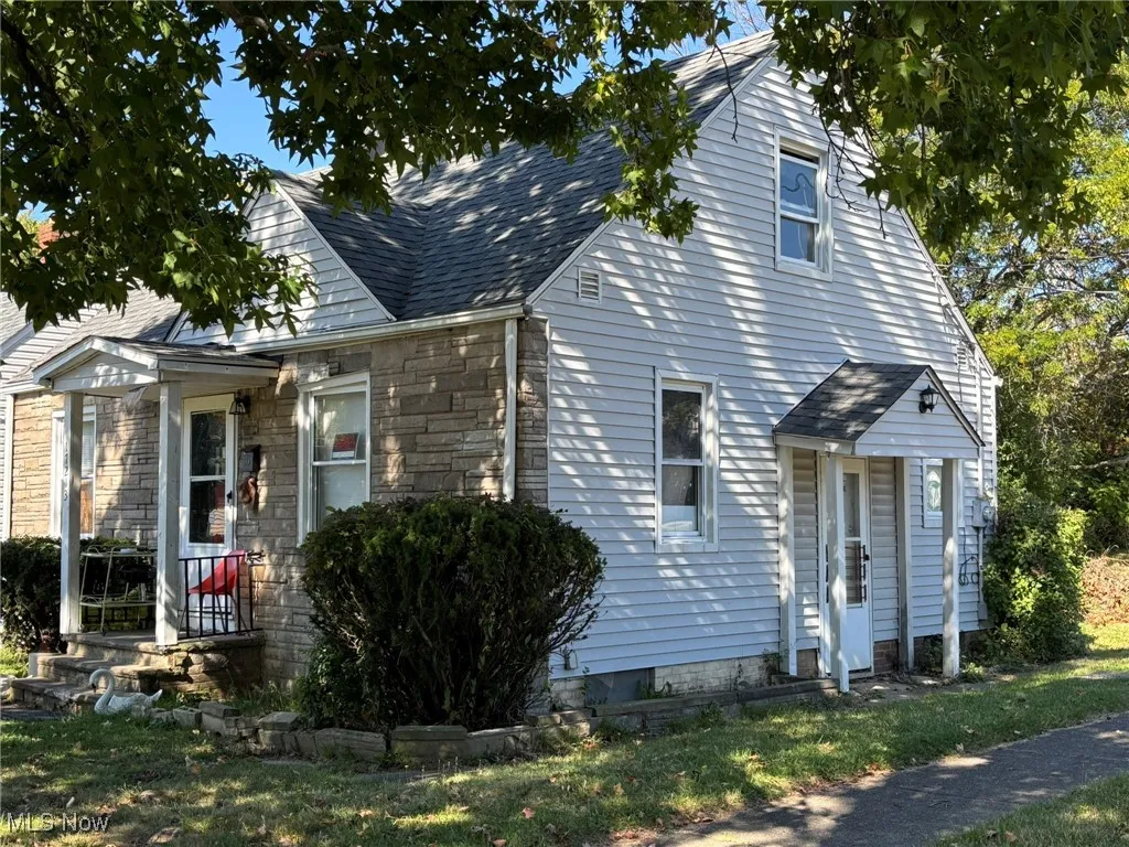 View of front of house with stone siding, roof with shingles, and a front lawn