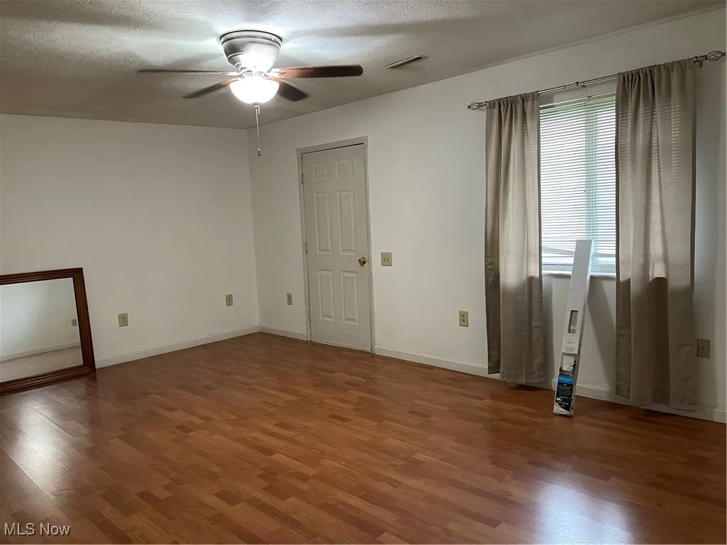 Living room with dark flooring, ceiling fan and front door.
