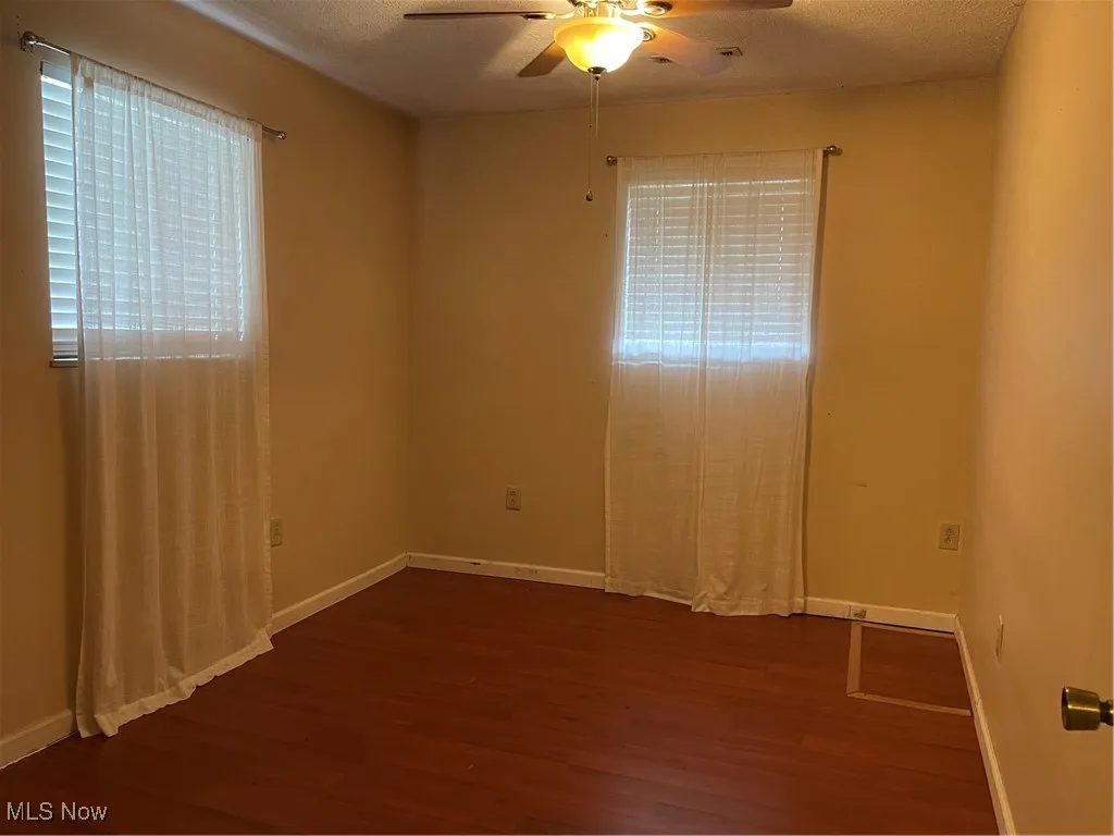 First bedroom with two windows and dark flooring.