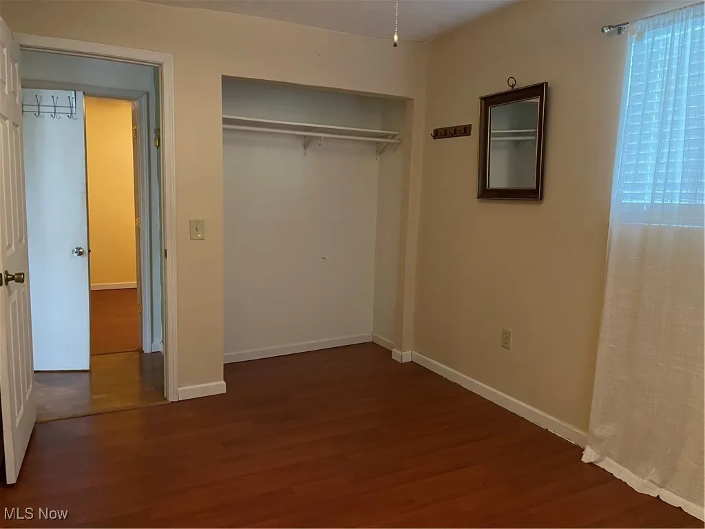 First bedroom with closet and dark flooring.