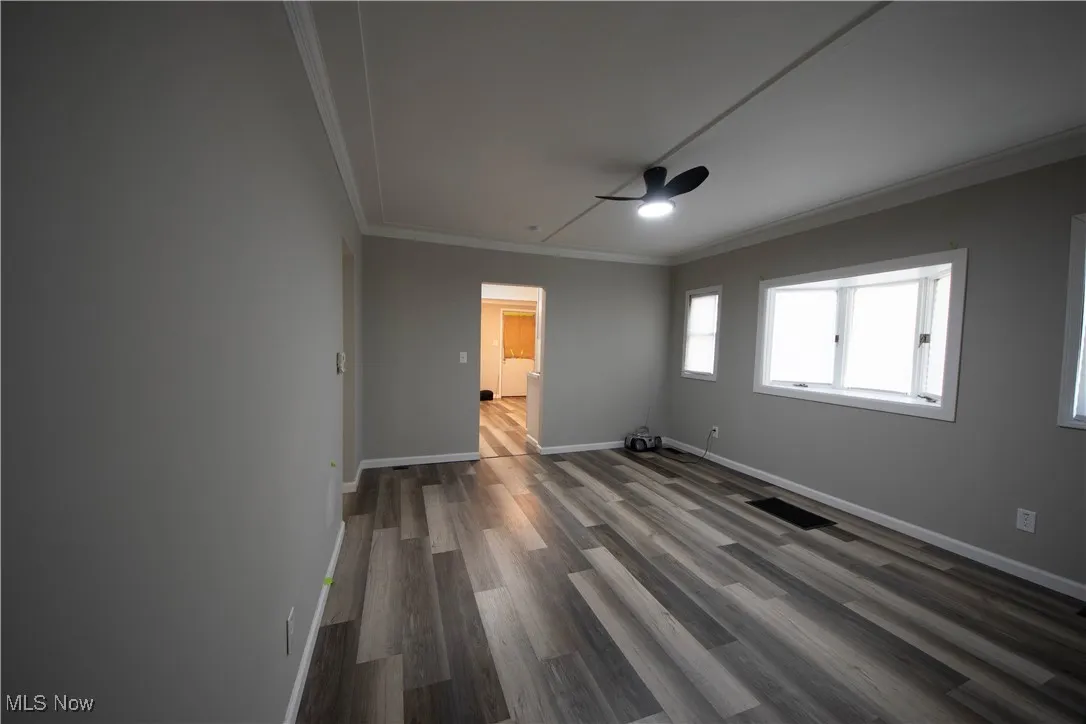Spare room featuring crown molding, dark wood-type flooring, and a ceiling fan