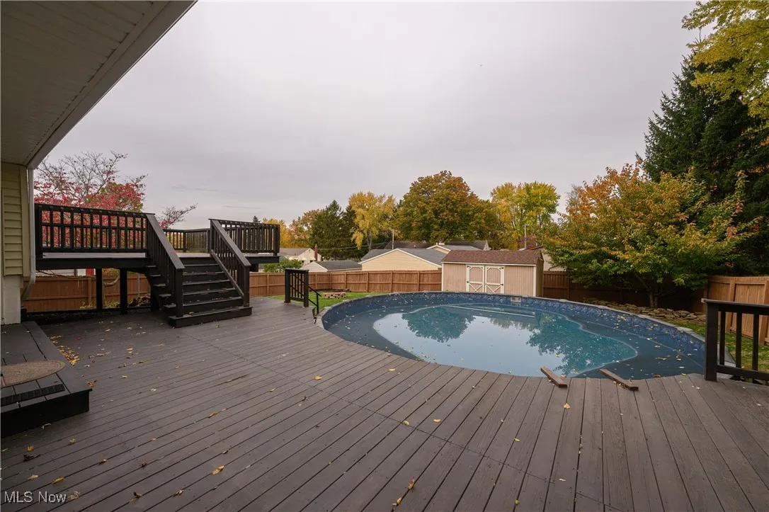 Outdoor pool with a wooden deck, a fenced backyard, a shed, and stairway